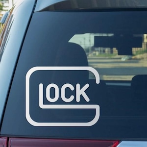 May include: White vinyl decal featuring the word "LOCK" inside a rounded rectangle. The decal is affixed to the rear window of a vehicle. The design is a stylized logo.