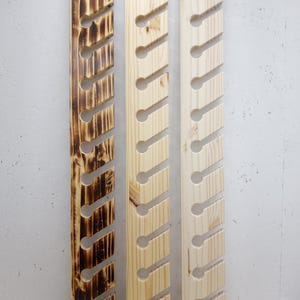 May include: Three vertical wooden wall racks featuring a series of angled slots with circular cutouts. The left rack has a dark, charred wood finish, while the center and right racks feature a natural, light-colored wood grain texture.