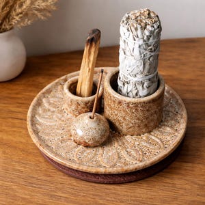 Puede incluir: Un juego de portaincienso de cerámica con un patrón floral decorativo. El juego incluye una bandeja redonda, dos pequeños soportes cilíndricos, un pequeño portaincienso redondo, un manojo de salvia blanca y un trozo de palo santo.