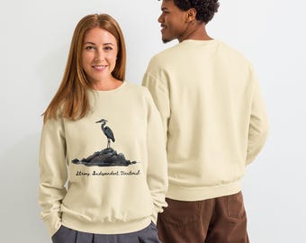 May include: Cream-colored sweatshirt featuring a watercolor illustration of a heron standing on a rock. Below the image is the text "Strong Independent Territorial". The sweatshirt is a unisex style.