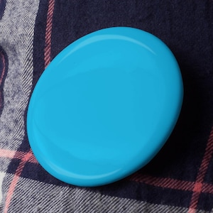 May include: A bright blue round disc with a smooth surface. The disc is on a plaid fabric background.