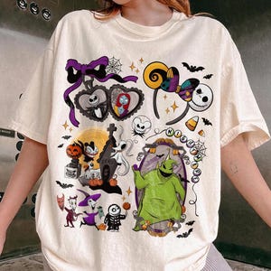 K&ouml;nnte beinhalten: Cremefarbenes T-Shirt mit einem farbenfrohen Grafikdesign mit Charakteren und Elementen aus "The Nightmare Before Christmas". Das Design umfasst Jack Skellington, Sally, Oogie Boogie und andere ikonische Bilder.