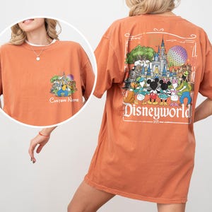 May include: Burnt orange t-shirt with a Disneyworld graphic on the back and a smaller graphic on the front. The back graphic features Disney characters and a castle. The front graphic has the text "Custom Name".