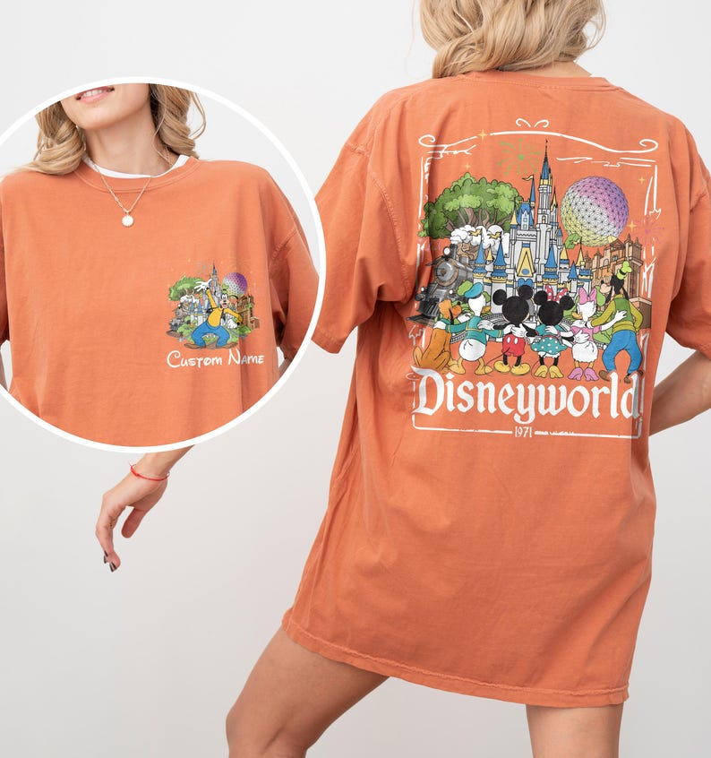 May include: Burnt orange t-shirt with a Disneyworld graphic on the back and a smaller graphic on the front. The back graphic features Disney characters and a castle. The front graphic has the text "Custom Name".