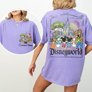 May include: A lilac-colored t-shirt featuring a Disney theme. The front has a Minnie Mouse graphic with the text "Custom Name". The back displays a colorful Disney World graphic with the text "Disneyworld" and the year "1971".