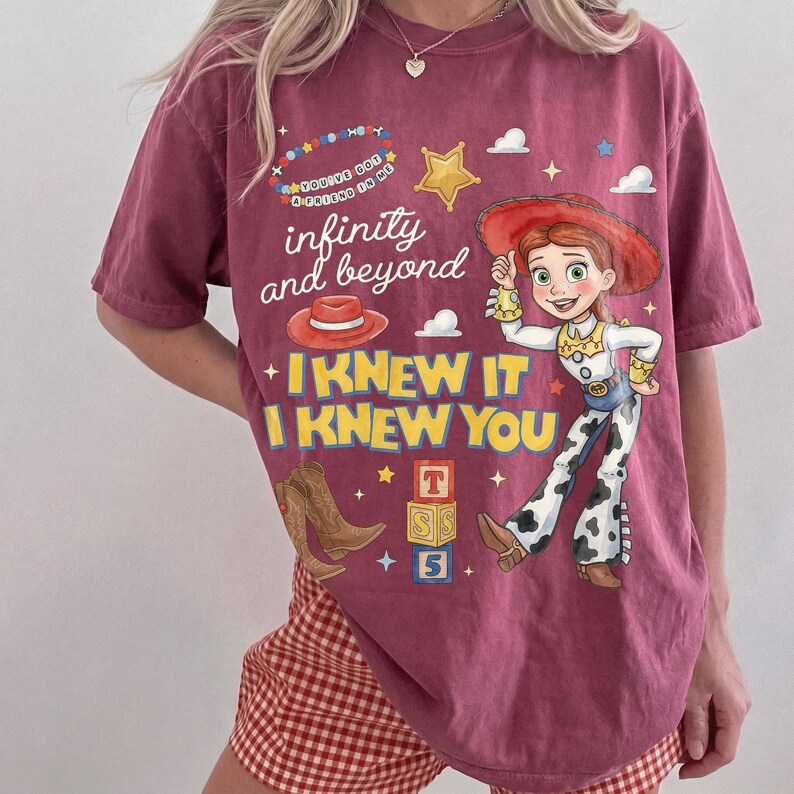 Pode incluir: Uma t-shirt de manga curta cor de vinho com um gr&aacute;fico de uma cowgirl, um chap&eacute;u vermelho, botas de cowboy castanhas e blocos de letras empilhados. O texto diz "infinity and beyond" e "I KNEW IT I KNEW YOU" com um c&iacute;rculo de contas.