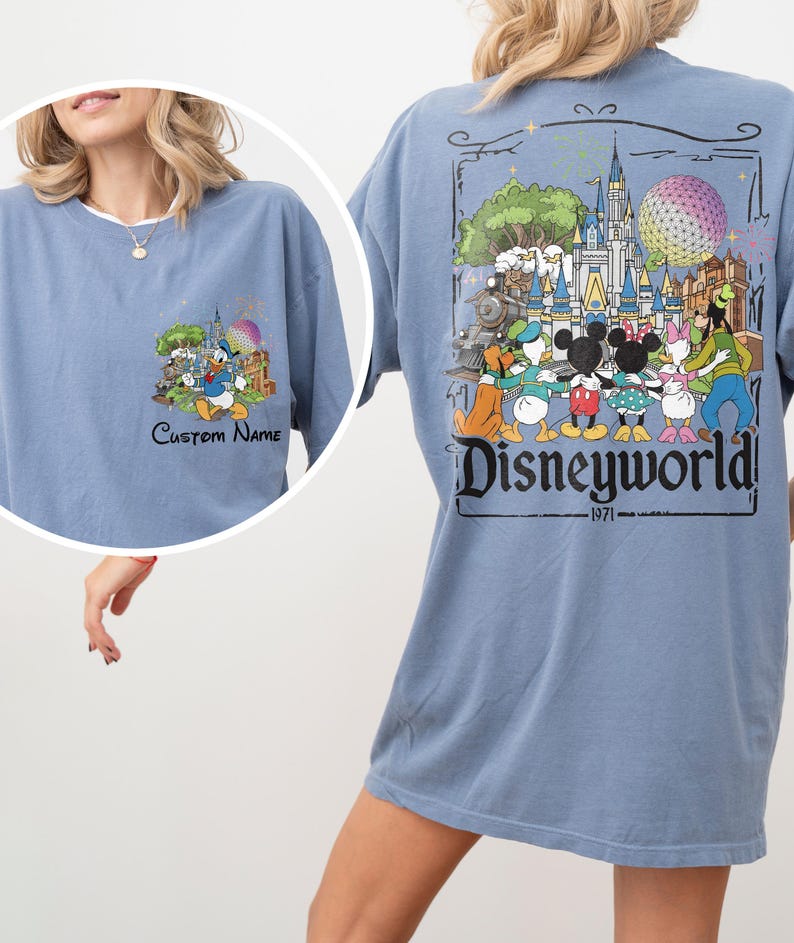 May include: A light blue t-shirt featuring a Disney World graphic. The front of the shirt has a small graphic with Donald Duck and the text "Custom Name". The back of the shirt has a larger graphic with Disney characters and the text "Disneyworld! 1971".