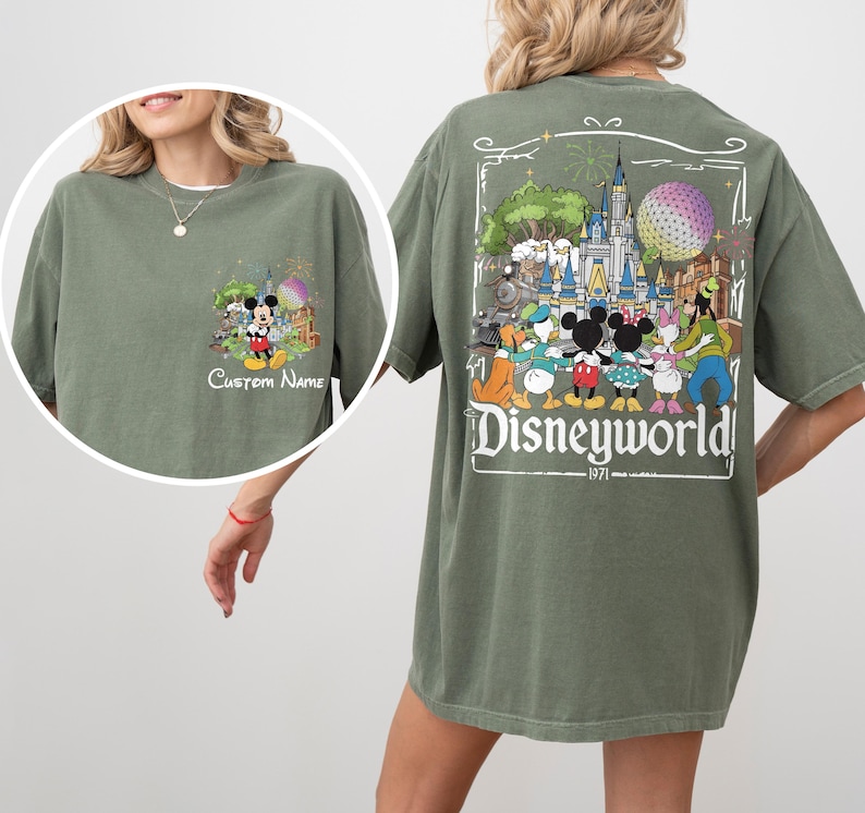 May include: Olive green t-shirt featuring a Disney World graphic on the back with Mickey Mouse and friends. The front has a smaller graphic with Mickey Mouse and the text "Custom Name".
