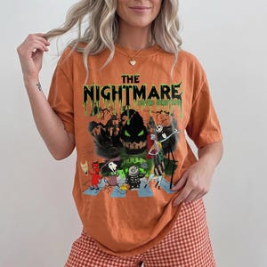 May include: Orange t-shirt featuring a graphic from "The Nightmare Before Christmas." The design includes the text "The Nightmare Before Christmas" in green, with characters like Jack Skellington and Sally. The shirt has short sleeves.
