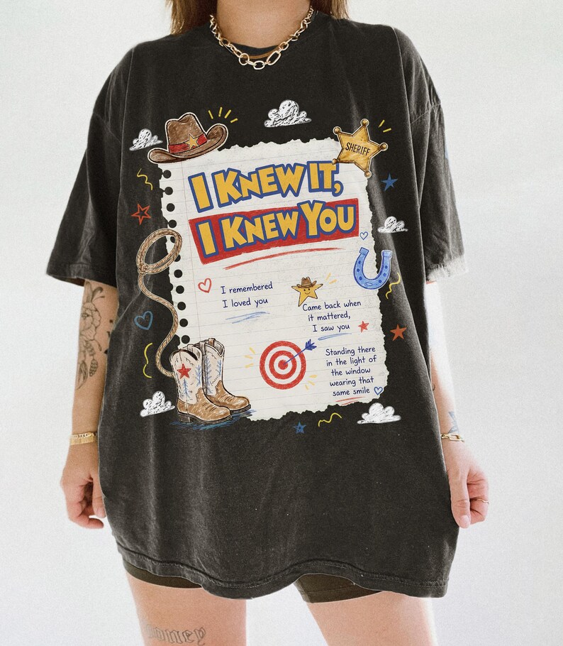 May include: A black t-shirt featuring a graphic print of a notebook page with the text I KNEW IT, I KNEW YOU. The design includes illustrations of a cowboy hat, a sheriff badge, a lasso, cowboy boots, a target, and various small decorative icons.