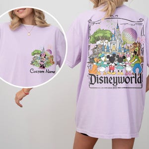May include: A light purple t-shirt featuring a front graphic of Minnie Mouse in front of a castle and fireworks, with the text "Custom Name". The back of the shirt has a large graphic of Disney characters and the text "Disneyworld 1971".