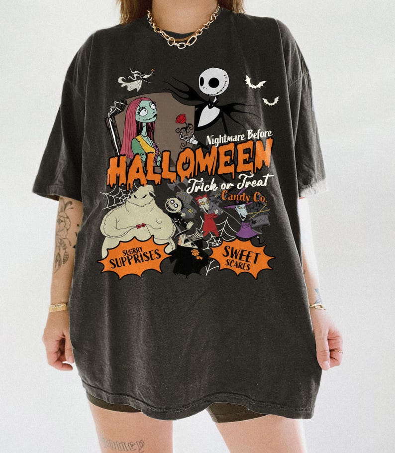 K&ouml;nnte beinhalten: Ein anthrazitfarbenes T-Shirt mit einem Grafikdruck der Charaktere aus Nightmare Before Christmas. Das Design zeigt Jack Skellington, Sally und Oogie Boogie mit dem Text Nightmare Before Halloween Trick or Treat Candy Co.