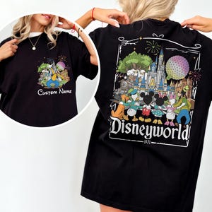 May include: Black t-shirt featuring a colorful Disney World graphic on the back, with the text "Disneyworld - 1971". The front of the shirt has a smaller graphic with the text "Custom Name". The design includes cartoon characters and fireworks.