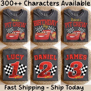 Op de afbeelding: Zes grijze t-shirts met race-thema ontwerpen. De shirts tonen teksten als "Mark's Pit Crew", "Birthday Boy" en namen met nummers. Elk ontwerp bevat een rode raceauto en geblokte vlaggen. De tekst "300++ Characters Available" staat bovenaan.