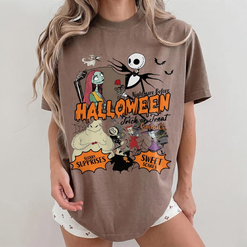 K&ouml;nnte beinhalten: Ein braunes Kurzarm-T-Shirt mit einem Grafikdruck von Charakteren aus Nightmare Before Christmas. Das Design enth&auml;lt den Text Nightmare Before HALLOWEEN Trick or Treat Candy Co. sowie Sugar Surprises und Sweet Scares.