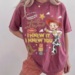 May include: A maroon short-sleeve t-shirt featuring a graphic of a cowgirl character, a red hat, brown cowboy boots, and alphabet blocks. The text reads: You've got a friend in me, infinity and beyond, I KNEW IT, I KNEW YOU, and T S 5.