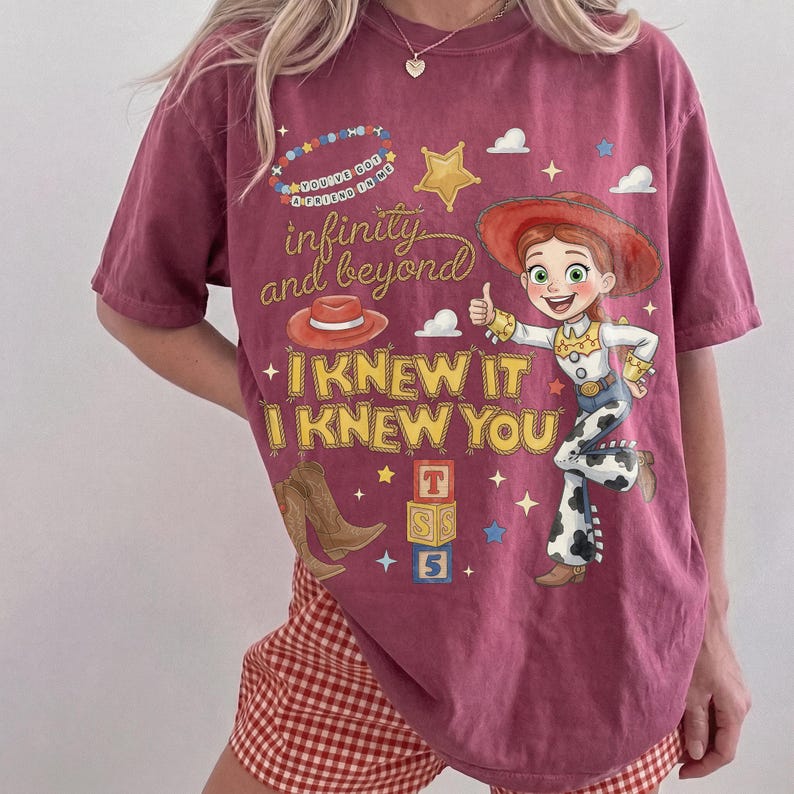 May include: A maroon short-sleeve t-shirt featuring a graphic of a cowgirl character, a red hat, brown cowboy boots, and alphabet blocks. The text reads: You've got a friend in me, infinity and beyond, I KNEW IT, I KNEW YOU, and T S 5.