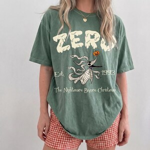 Op de afbeelding: Groen t-shirt met het woord "ZERO" in een druipend lettertype, met een illustratie van Zero uit "The Nightmare Before Christmas". Het shirt bevat ook de tekst "Est. 1993" en "The Nightmare Before Christmas."