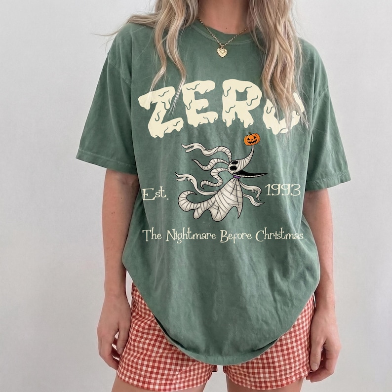 Op de afbeelding: Groen t-shirt met het woord "ZERO" in een druipend lettertype, met een illustratie van Zero uit "The Nightmare Before Christmas". Het shirt bevat ook de tekst "Est. 1993" en "The Nightmare Before Christmas."