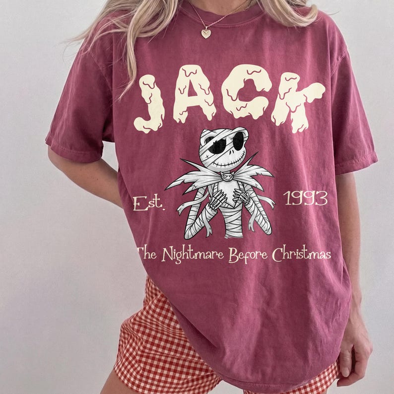 Op de afbeelding: Bordeauxrood t-shirt met een afbeelding van Jack Skellington uit "The Nightmare Before Christmas". Het ontwerp bevat het woord "JACK", het personage en de tekst "Est. 1993."