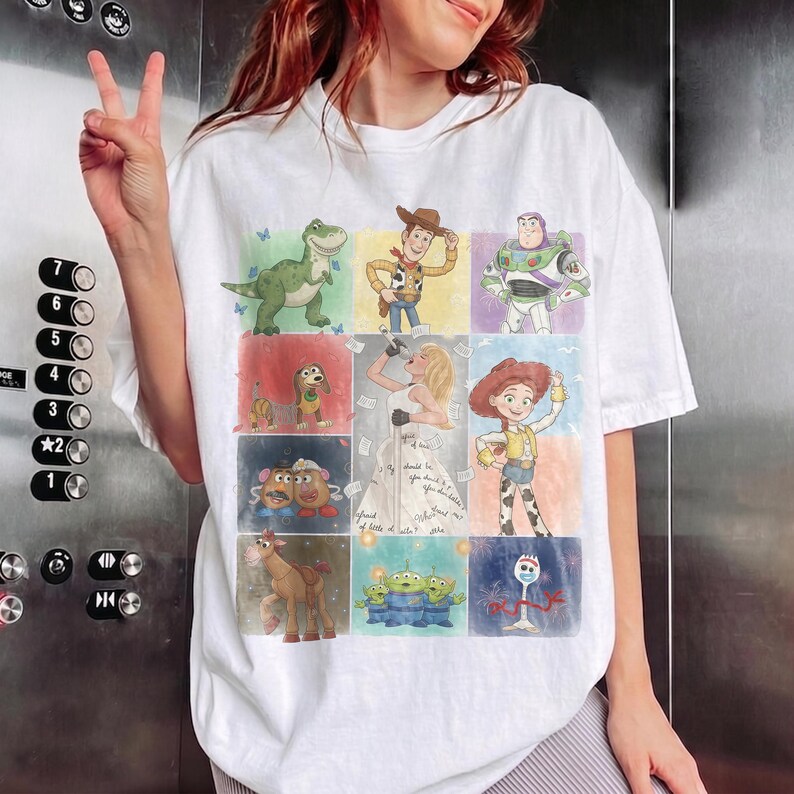 K&ouml;nnte beinhalten: Ein wei&szlig;es T-Shirt mit kurzen &Auml;rmeln, das ein Raster aus farbenfrohen Illustrationen verschiedener animierter Figuren aus der Toy Story-Reihe zeigt, darunter Woody, Buzz Lightyear, Jessie, Rex, Slinky Dog, Mr. und Mrs. Potato Head, Bullseye und Forky.