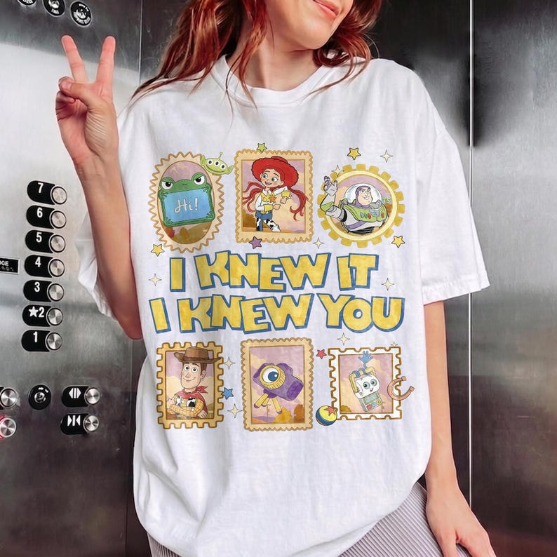 May include: A white t-shirt featuring a graphic print of Toy Story characters in postage stamp-style frames, including Rex, Jessie, Buzz Lightyear, Woody, and others. The text "I KNEW IT I KNEW YOU" is printed in large yellow letters across the center.