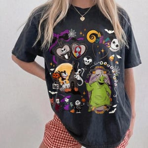 K&ouml;nnte beinhalten: Dunkelgraues T-Shirt mit einer Collage von Charakteren aus "The Nightmare Before Christmas". Das Design umfasst Jack Skellington, Sally, Zero und Oogie Boogie, mit Halloween-Akzenten wie Flederm&auml;usen und Spinnweben.