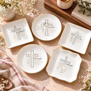 Puede incluir: Cinco platos de cerámica blanca con bordes dorados, que presentan ilustraciones de cruces negras y nombres personalizados como Matthew, James, Sophia, Ashley y Ophie, junto con textos e imágenes religiosas inspiradoras.