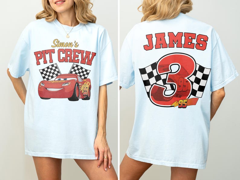Op de afbeelding: Lichtblauw T-shirt met een rode raceauto-afbeelding en de tekst "Simon's PIT CREW" op de voorkant. De achterkant van het shirt toont de naam "JAMES" boven een groot rood nummer "3" met geblokte vlaggen en het nummer "95".