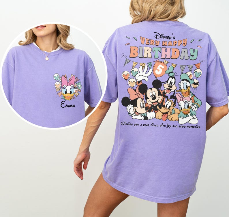 Puede incluir: Una camiseta de color lila claro con personajes de Disney. La parte delantera presenta a Daisy Duck y el nombre "Emma". La parte trasera muestra "Disney's Very Happy Birthday" con Mickey, Minnie, Donald, Goofy y Pluto. La camiseta tiene un corte holgado.