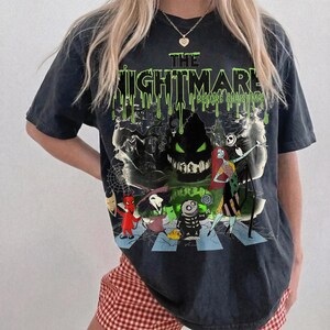 May include: Dark gray t-shirt featuring a graphic from "The Nightmare Before Christmas." The design includes the text "THE NIGHTMARE BEFORE CHRISTMAS" in green dripping letters, along with characters like Jack Skellington and Sally.
