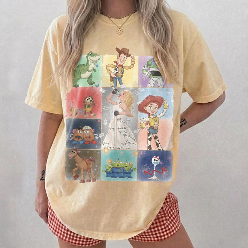 K&ouml;nnte beinhalten: Ein blassgelbes Kurzarm-T-Shirt mit einem Raster aus neun farbenfrohen Illustrationen animierter Figuren aus der Toy Story-Filmreihe, darunter Woody, Buzz Lightyear, Jessie, Rex, Slinky Dog, Mr. und Mrs. Potato Head, Bullseye und Forky.