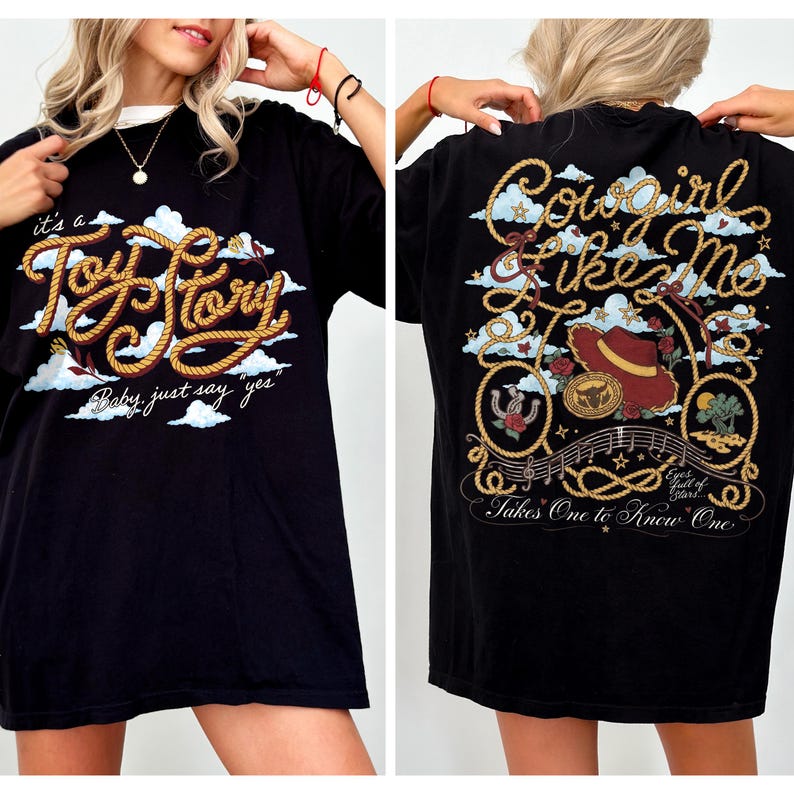 Op de afbeelding: Een zwart t-shirt met een voorzijde voorzien van touwachtige tekst "it's a Toy Story Baby, just say yes" en een achterzijde met de tekst "Cowgirl like Me" en "Takes One to Know One" inclusief een hoed en een hoefijzer als afbeelding.