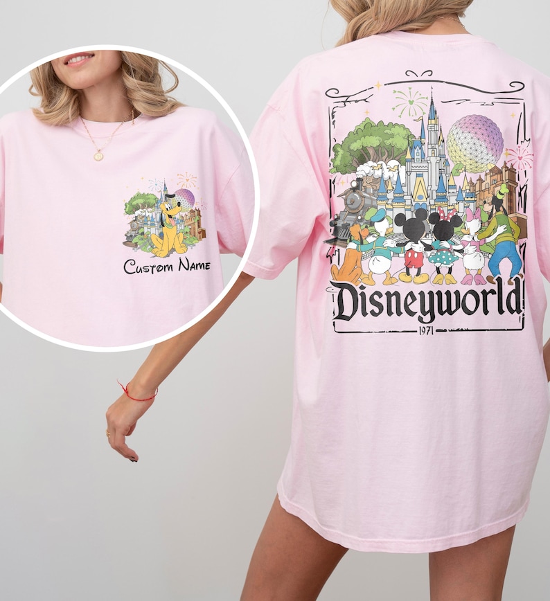 May include: Light pink t-shirt featuring a Disney World graphic on the back and a smaller graphic on the front. The back graphic includes the text "Disneyworld 1971" and various Disney characters. The front graphic has Pluto and the text "Custom Name".