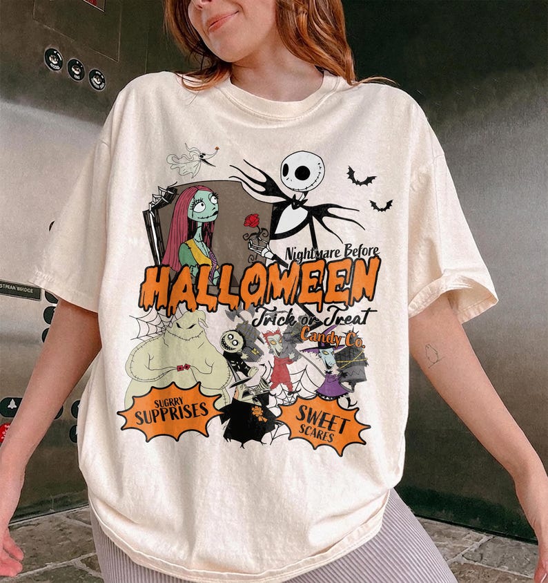 K&ouml;nnte beinhalten: Ein cremefarbenes Kurzarm-T-Shirt mit einem Grafikdruck der Figuren aus Nightmare Before Christmas. Das Design enth&auml;lt den Text Halloween, Trick or Treat, Candy Co., Sugry Surprises und Sweet Scares.