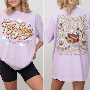 Op de afbeelding: Een lichtpaars t-shirt met een afbeelding op de voorkant in touwstijl met de tekst "it's a Toy Story Baby, just say yes" en een achterkant met de tekst "Cowgirl like Me" en "Takes One to Know One" gecombineerd met western-motieven.
