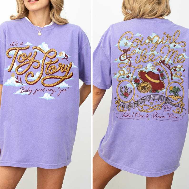 Op de afbeelding: Een lichtpaars t-shirt met een afbeelding op de voorkant met touwachtige tekst "it's a Toy Story Baby, just say "yes"" en een afbeelding op de achterkant met touwranden, een cowboyhoed, een riemgesp en de tekst "Cowgirl like Me".