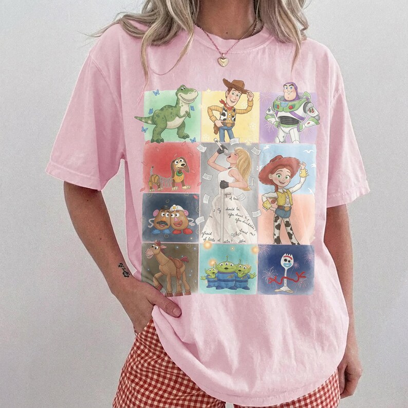 K&ouml;nnte beinhalten: Ein hellrosa T-Shirt mit kurzen &Auml;rmeln und einem Raster aus farbenfrohen Illustrationen verschiedener Zeichentrickfiguren, darunter ein gr&uuml;ner Dinosaurier, ein Cowboy, ein Weltraum-Ranger, ein Hund, eine Kartoffelfigur, ein Cowgirl, ein Pferd und Aliens.