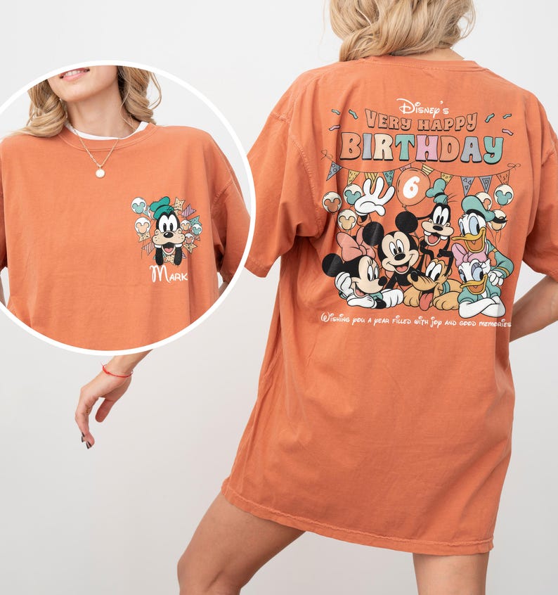 Puede incluir: Una camiseta naranja con personajes de Disney. La parte delantera tiene una caricatura de Goofy con el nombre "MARK". La parte trasera muestra "Disney's Very Happy Birthday" con Mickey, Minnie, Donald, Daisy y Goofy. La camiseta tiene cuello redondo y mangas cortas.
