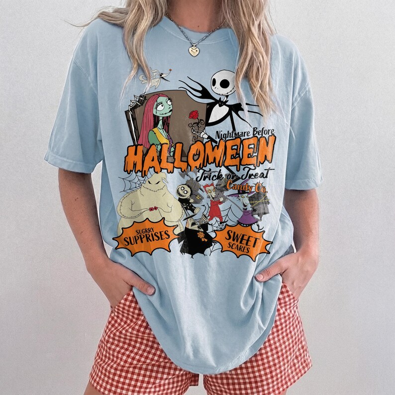 K&ouml;nnte beinhalten: Ein hellblaues T-Shirt mit einem Grafikdruck der Figuren aus Nightmare Before Christmas, darunter Jack Skellington und Sally. Der Text lautet Nightmare Before Halloween, Trick or Treat Candy Co, Sugary Surprises und Sweet Scares.