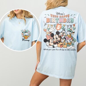 Puede incluir: Camisetas de color azul claro con personajes de Disney. Una camiseta presenta a Pato Donald con la palabra "Mommy". La otra camiseta tiene un gr&aacute;fico de Mickey y Minnie Mouse, Goofy, Pato Donald y Daisy, y el texto "Disney's Very Happy Birthday".