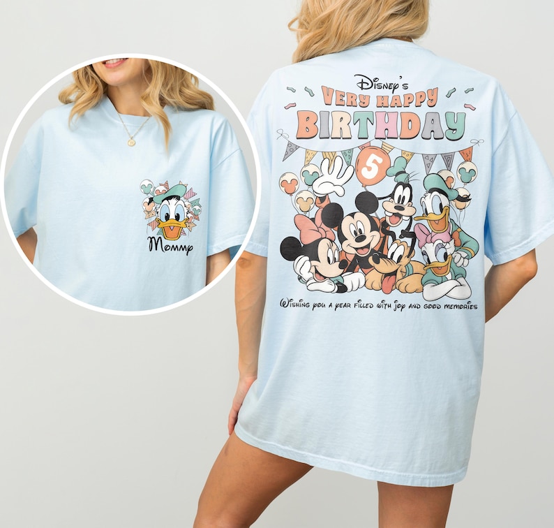 Puede incluir: Camisetas de color azul claro con personajes de Disney. Una camiseta presenta a Pato Donald con la palabra "Mommy". La otra camiseta tiene un gr&aacute;fico de Mickey y Minnie Mouse, Goofy, Pato Donald y Daisy, y el texto "Disney's Very Happy Birthday".