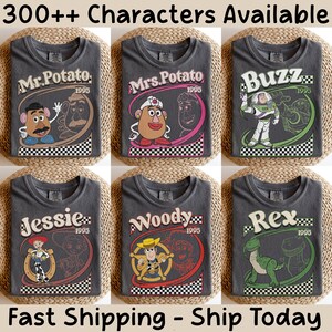 May include: Six charcoal gray t-shirts featuring Toy Story characters: Mr. Potato Head, Mrs. Potato Head, Buzz Lightyear, Jessie, Woody, and Rex. Each shirt has a character graphic with the year 1995 and a checkered border. The text "300++ Characters Available" is at the top.