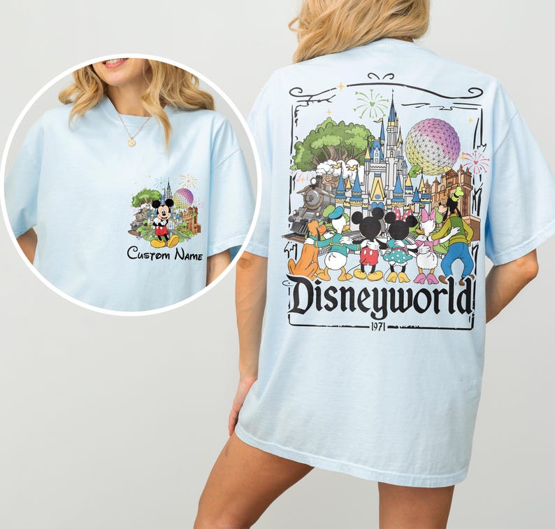 May include: Light blue t-shirt featuring a colorful Disneyworld graphic on the back and a smaller Mickey Mouse design on the front. The back graphic includes the text "Disneyworld" and "1971".