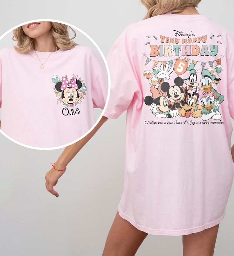 Puede incluir: Camiseta rosa claro con Minnie Mouse y el nombre "Olivia" en la parte delantera. La parte trasera de la camiseta muestra personajes de Disney con el texto "Disney's Very Happy Birthday" y "Wishing you a year filled with joy and good memories."