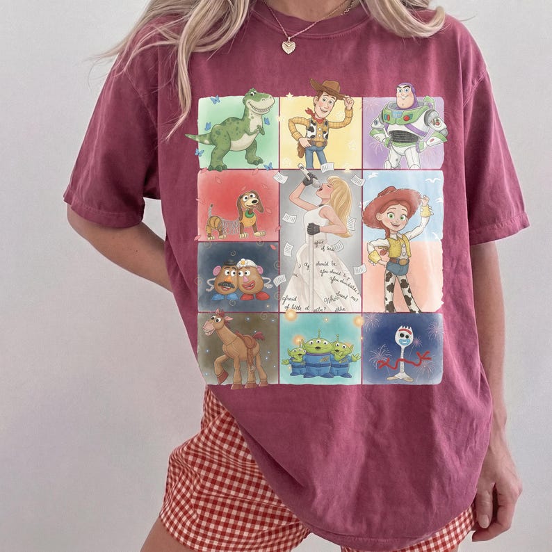 K&ouml;nnte beinhalten: Ein dunkelrotes Kurzarm-T-Shirt mit einem Raster aus Toy Story-Figuren, darunter Rex, Woody, Buzz Lightyear, Slinky Dog, Mr. und Mrs. Potato Head, Bullseye, die Aliens und Forky, um eine zentrale Illustration einer S&auml;ngerin in einem Kleid.