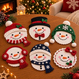 May include: A set of six round crochet snowman coasters, each featuring a white face with a carrot nose, black eyes, and a stitched smile. The snowmen are decorated with various winter accessories including red and blue scarves, hats, and bows.