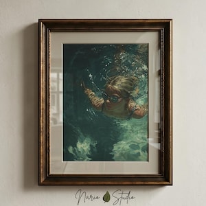 May include: A framed wall art print featuring an illustration of a person swimming underwater while wearing dark goggles. The artwork is encased in a dark brown wooden frame with a light-colored mat border, displaying deep green and blue water tones.