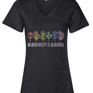 Peut inclure: T-shirt noir à col en V avec un motif floral coloré et le texte blanc "Neurodiversité est belle". Les fleurs sont dessinées en rouge, jaune, vert, bleu et rose. Un vêtement décontracté.