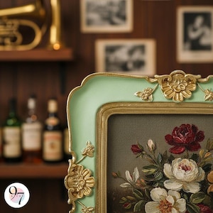 A close-up of the bottom right corner of a light green square picture frame with gold ornate details, showing a painting of red and white flowers.